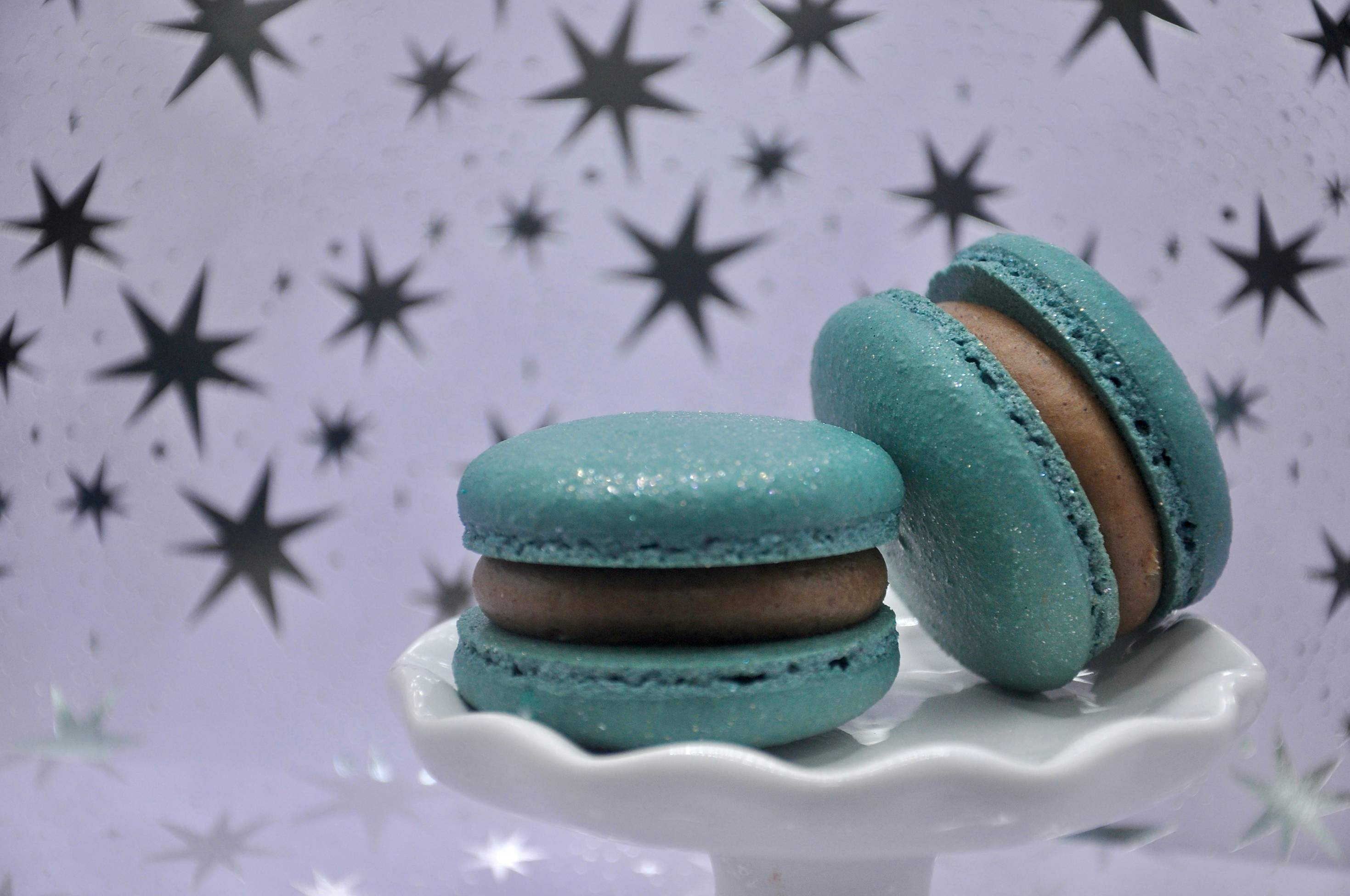 Two blue macaroons sitting on top of a white cake plate