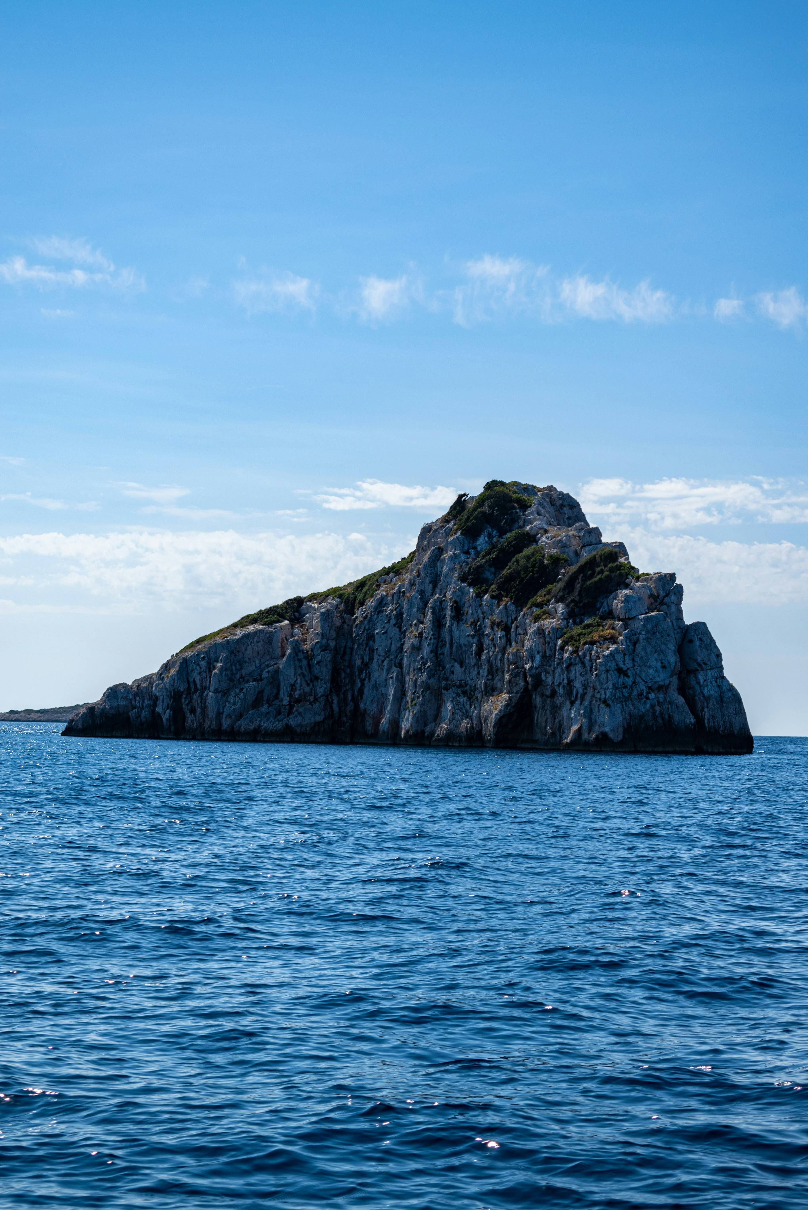 brown and green rock formation on sea under blue sky during daytime