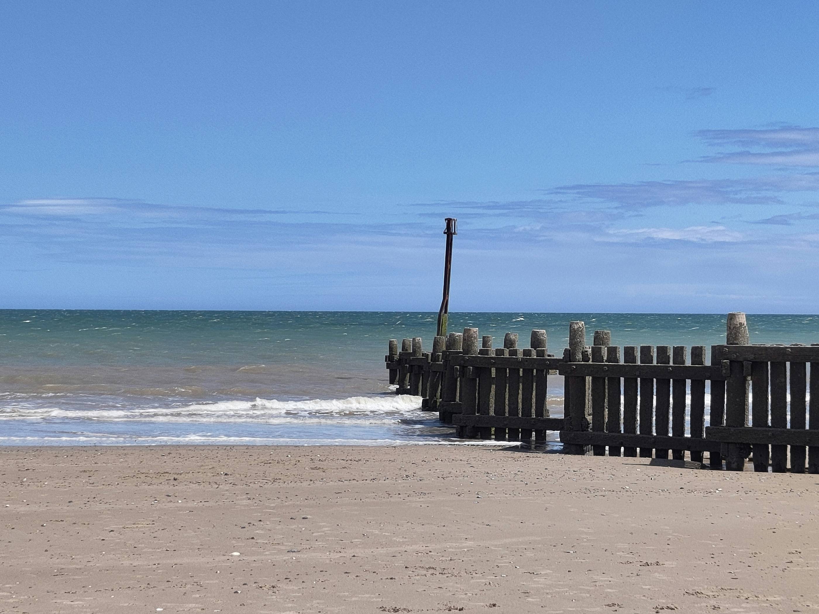 The ocean meets the beach with wooden structure.